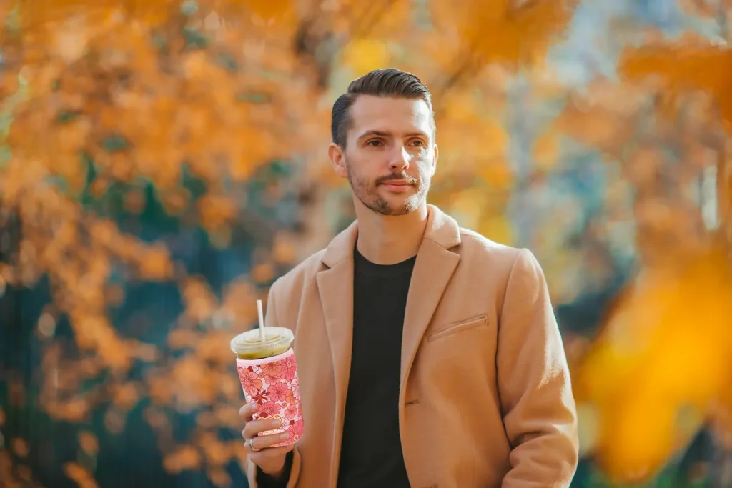 Premium custom sublimation neoprene coffee sleeve held by a man in a beige coat, autumn lifestyle setting.