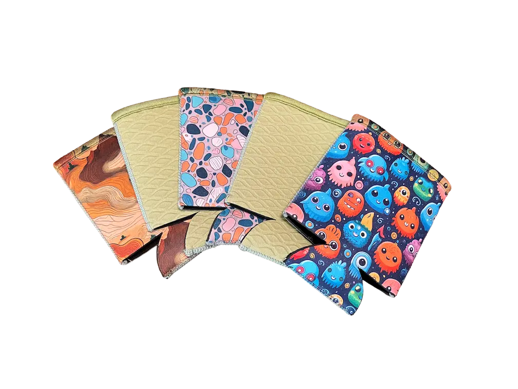 Finished custom neoprene can koozies with vibrant sublimation patterns including monsters and desert maps, demonstrating the 100% color vibrancy achievable on our factory-direct blanks.