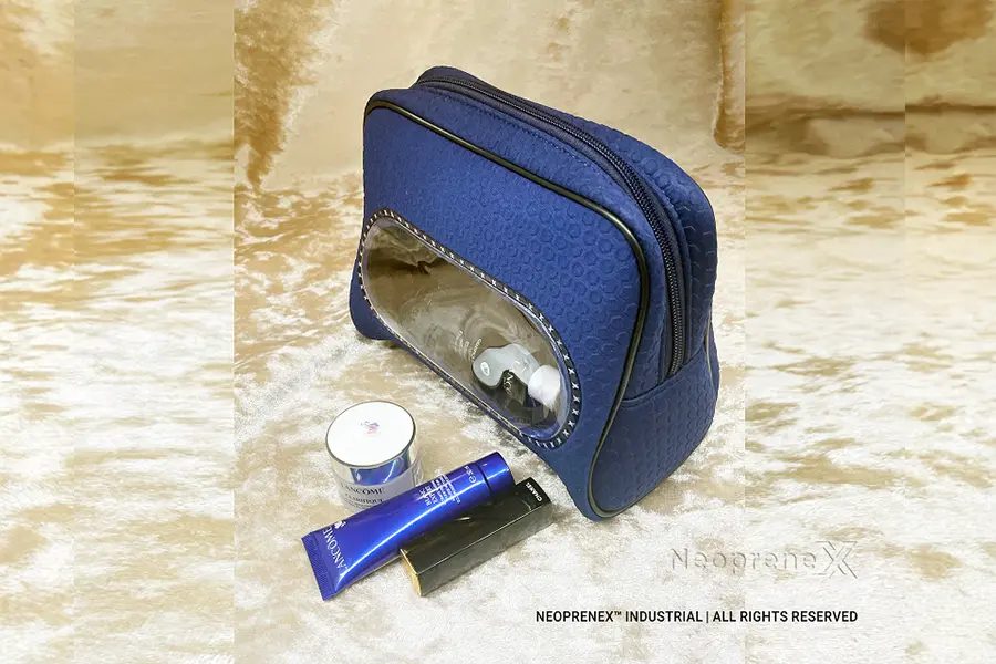 Stand-up navy neoprene makeup bag with front transparent window styled with cosmetic jars and tubes on a gold backdrop