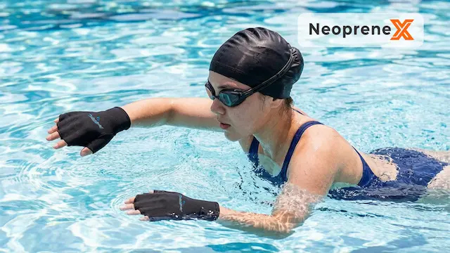 A female swimmer wearing NeopreneX black half-finger neoprene swim gloves training in a sunny swimming pool. This demonstrates the enhanced water resistance, snug ergonomic fit, and premium durability of our custom webbed swimming gloves for water fitness.
